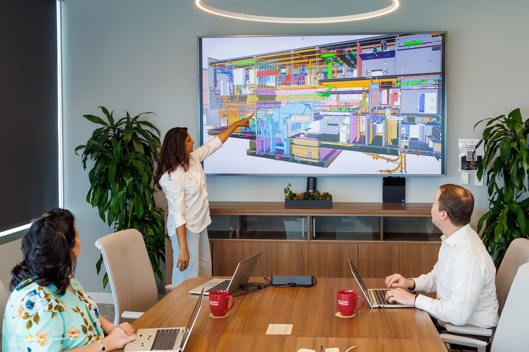 Three McCownGordon associates having a meeting and looking at a Building Information Model that a woman is pointing at on the screen